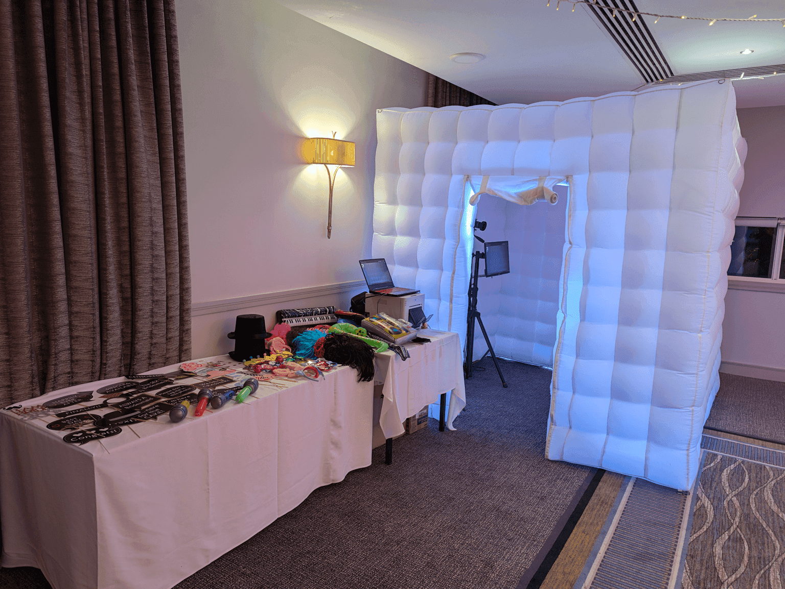 White inflatable photo booth with pink interior lighting set up at an event, with a props table alongside